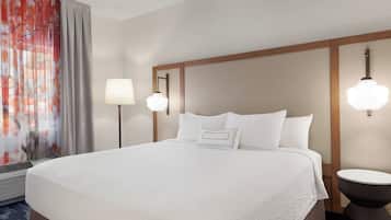 Una habitación de hotel con una cama grande, dos lámparas de noche, una mesa redonda y una ventana con cortinas.