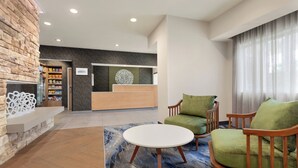 A lobby with a reception desk, green armchairs, a white coffee table, and a stone wall. - Fairfield Inn by Marriott Visalia Sequoia (Visalia)