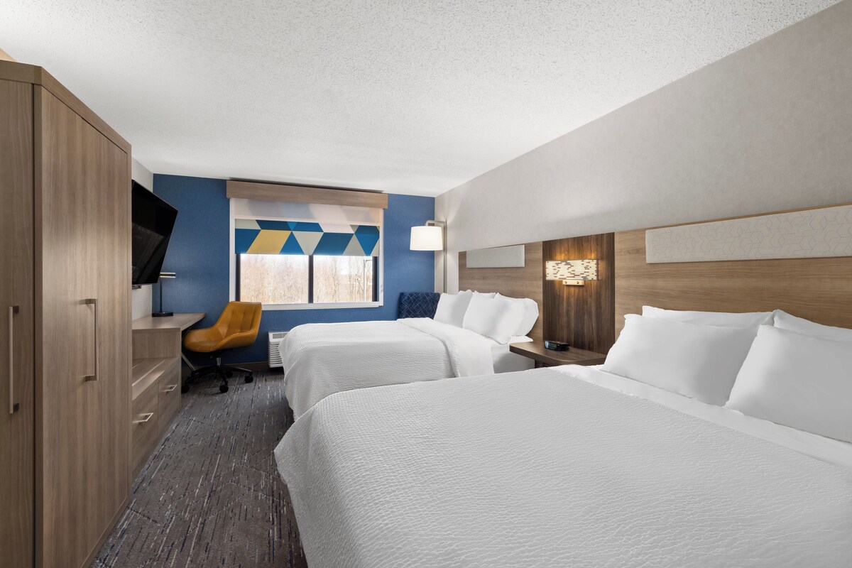 A hotel room with two beds, a desk, a chair, and a TV.
