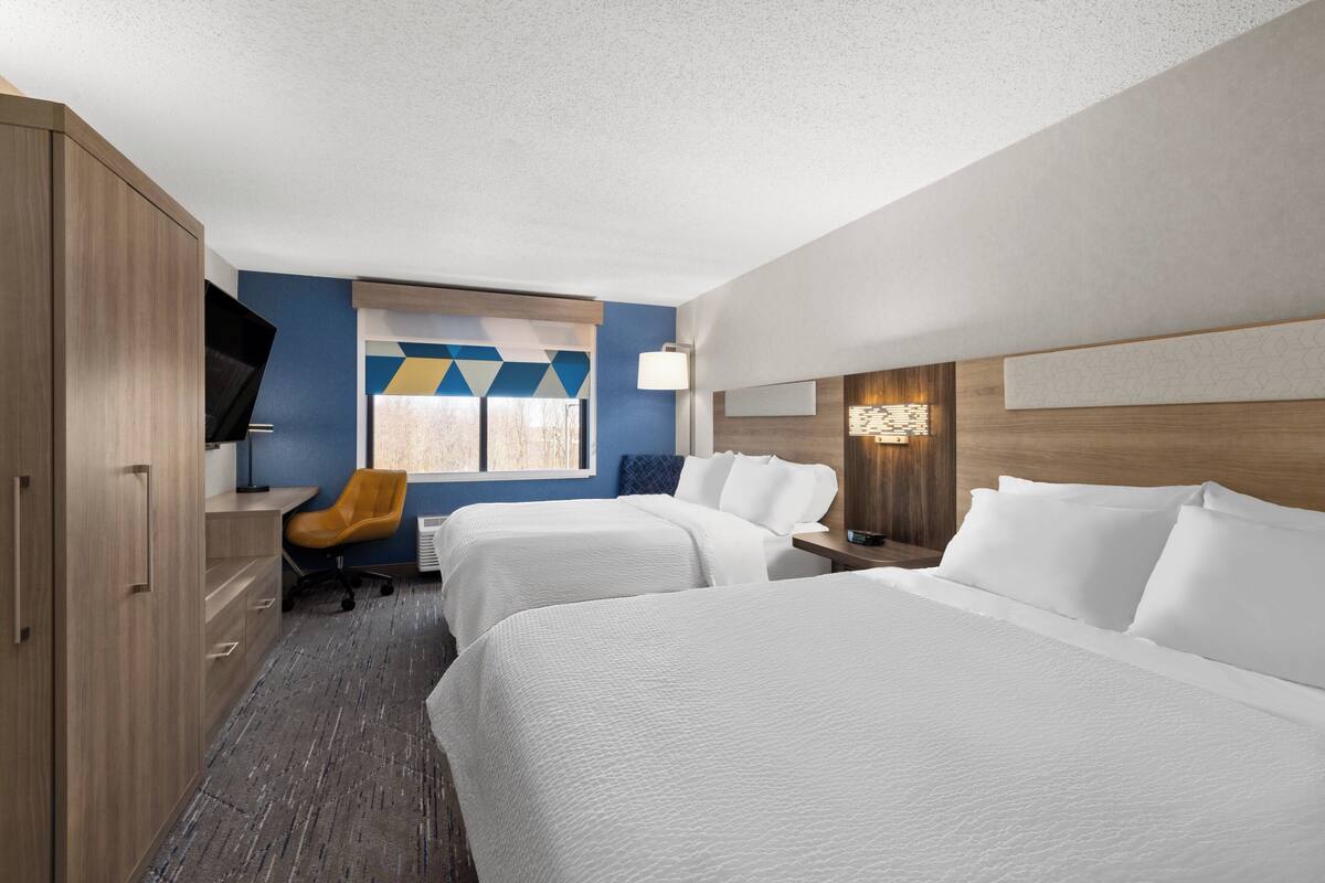 A hotel room with two beds, a desk, a chair, and a TV.