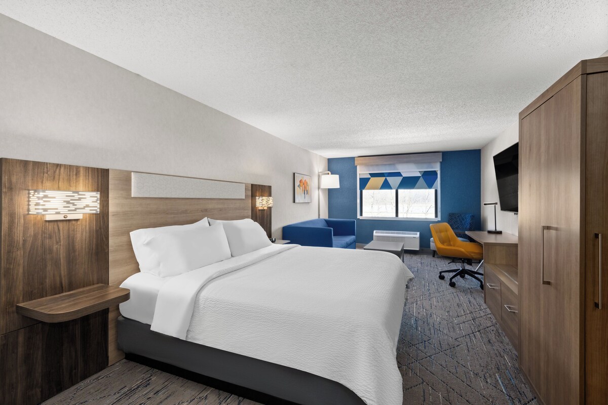 A hotel room with a bed, a desk, a chair, a TV, and a window.