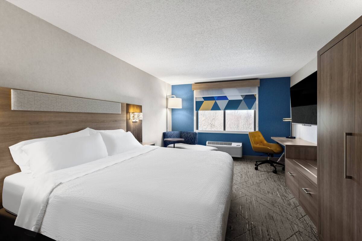 A hotel room with a large bed, a desk, a chair, a TV, and a window with a view.