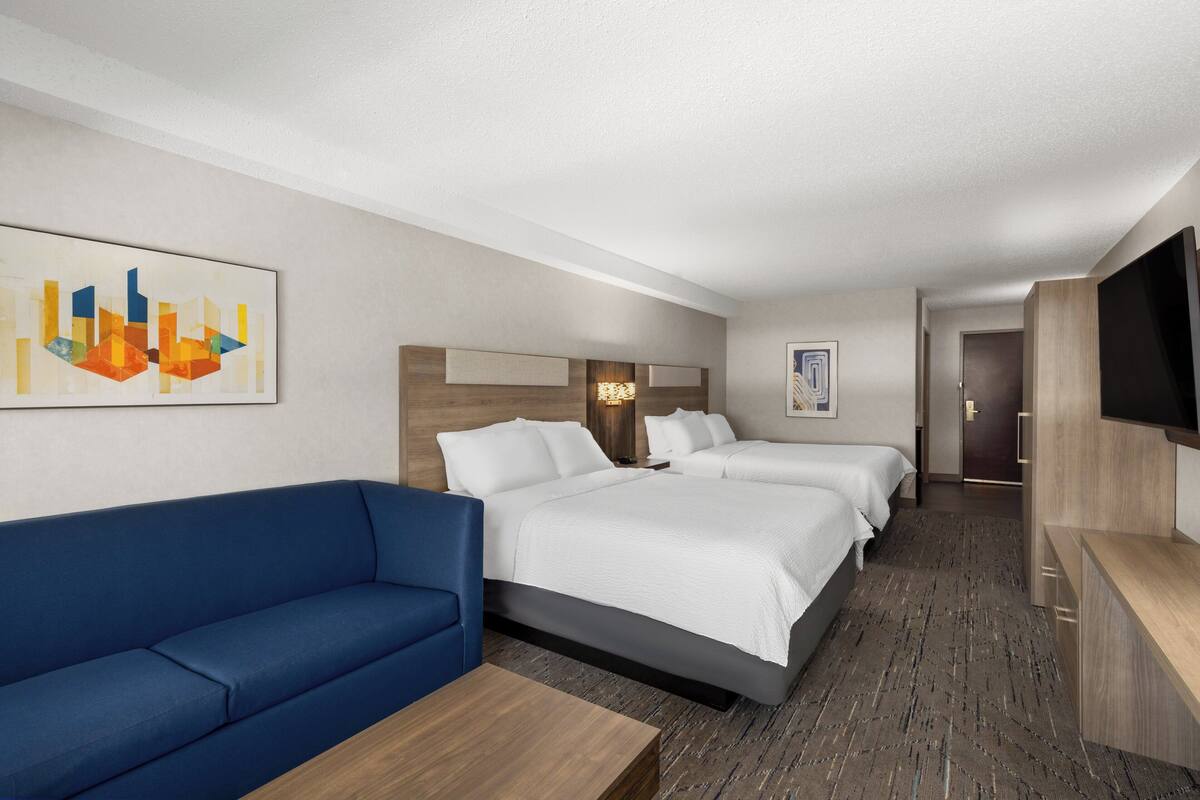 A hotel room with a large bed, a blue sofa, a TV, and artwork on the walls.