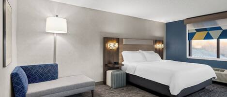 Ein Hotelzimmer mit einem Bett, einer Bank, einer Wandlampe und einem Fenster mit Ausblick.