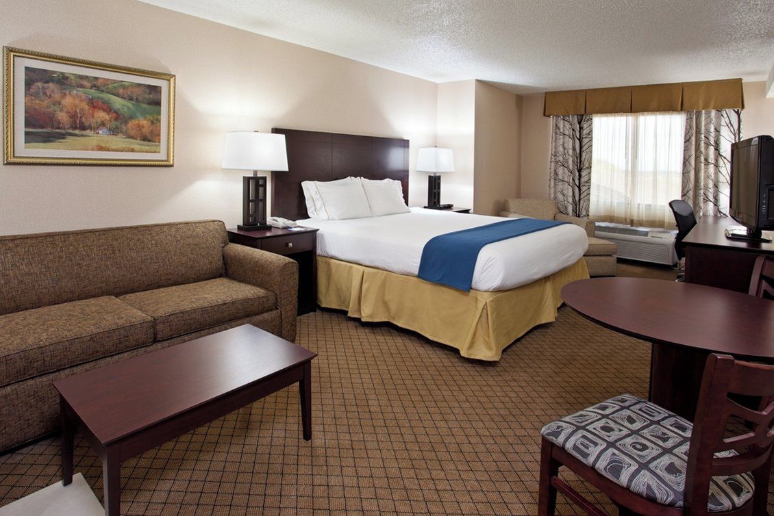 A hotel room with a bed, a sofa, a desk, a chair, and a television.