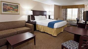 A hotel room with a bed, a sofa, a desk, a chair, and a television.