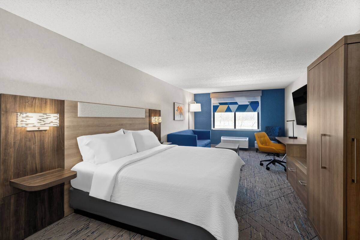 A modern hotel room with a large bed, a desk, a chair, and a wardrobe.
