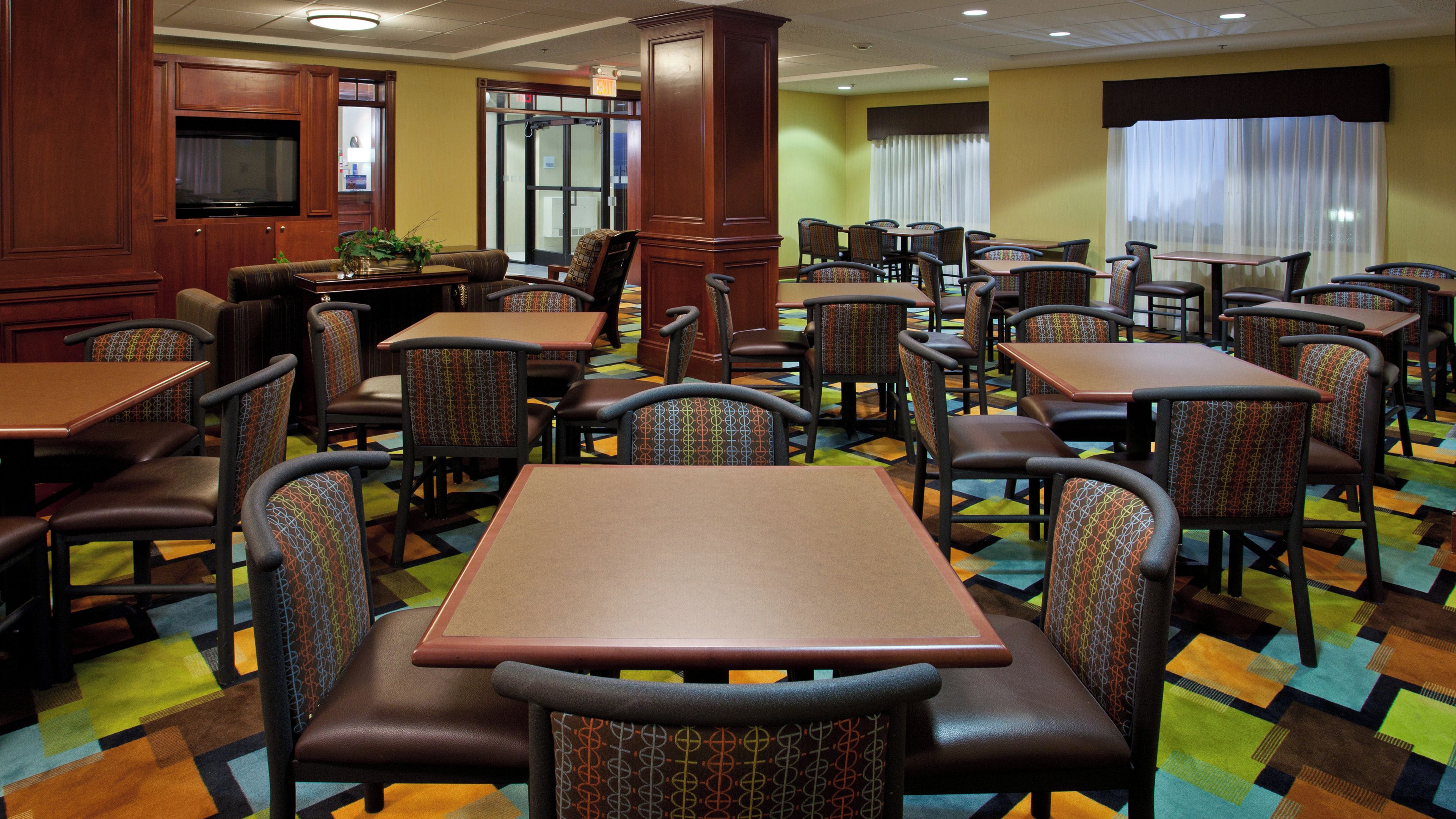 A hotel dining area with multiple tables and chairs, a television, and a patterned carpet.