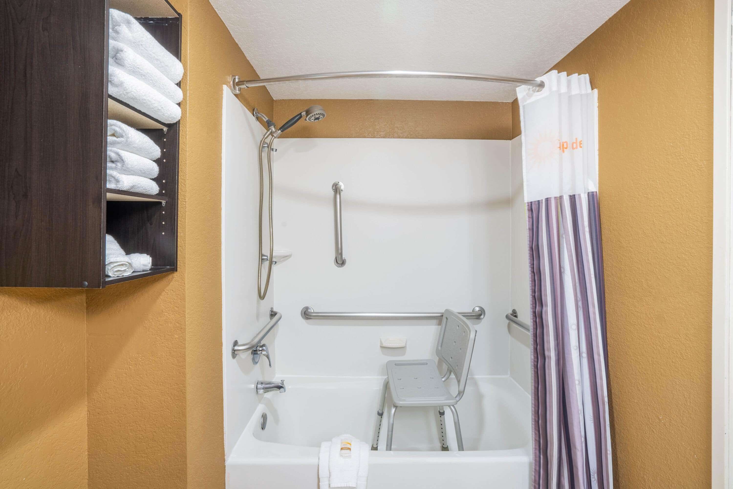 Un baño con bañera, ducha, barra de apoyo, toallero y cortina de ducha a rayas.