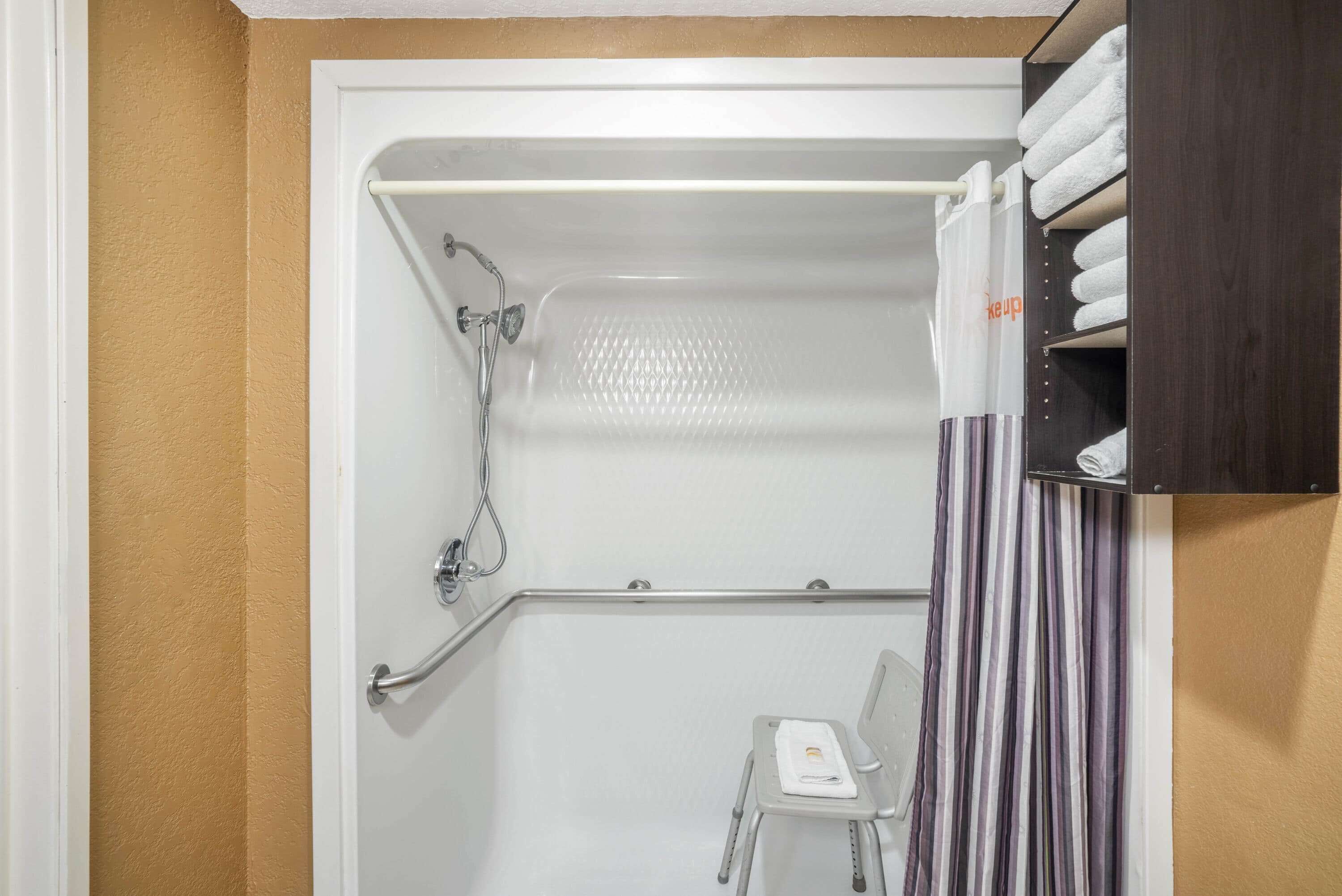 A shower area with a white bathtub, a showerhead, a grab bar, a towel rack, and a striped curtain.