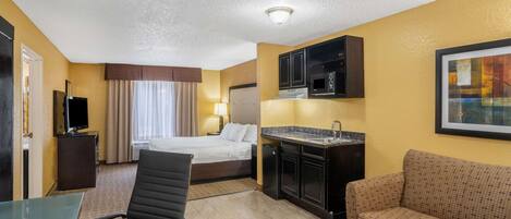 A hotel room with a bed, a desk, a chair, a sofa, a kitchenette, and a TV.
