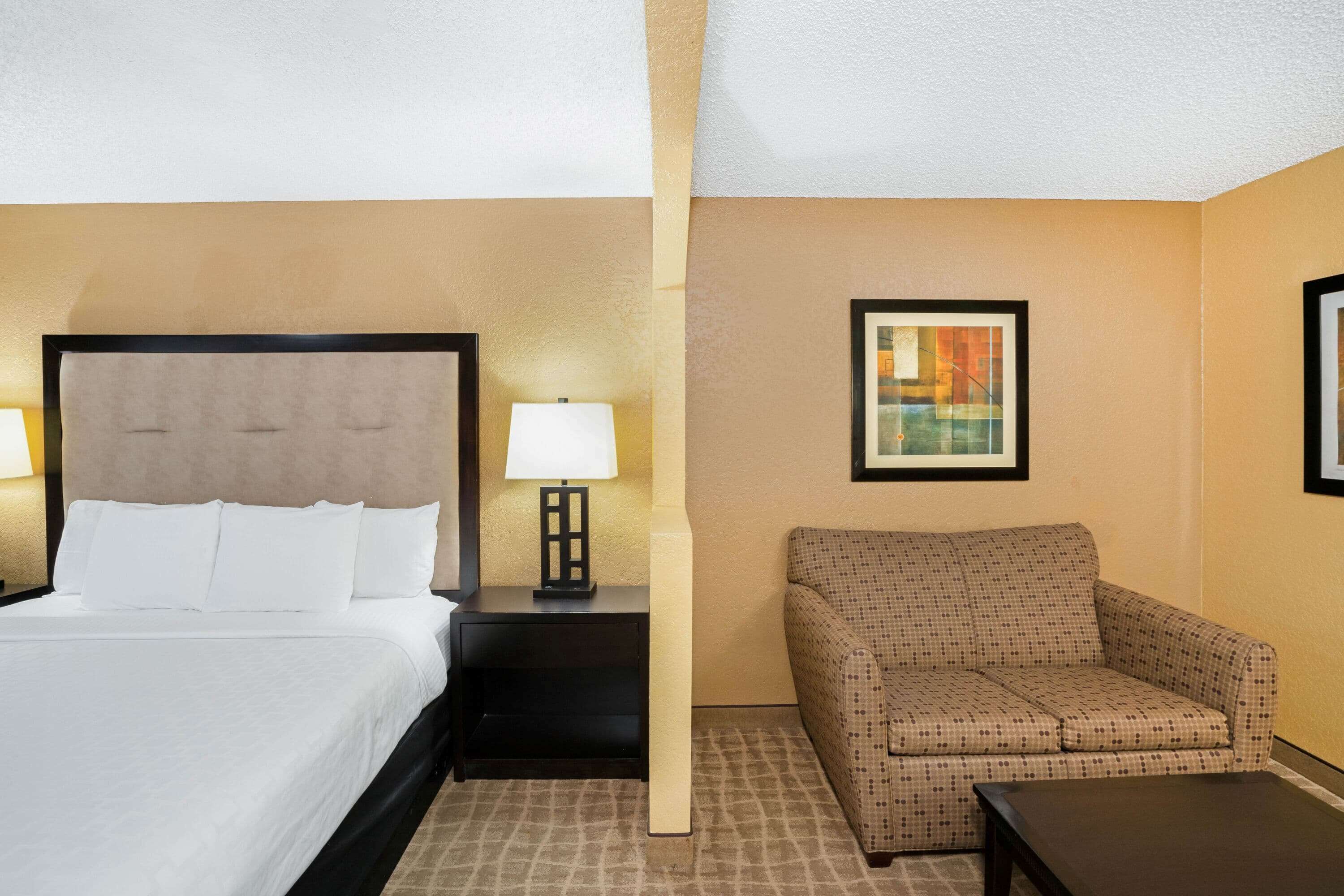 A hotel room with a bed, a nightstand with a lamp, a sofa, and a framed picture on the wall.