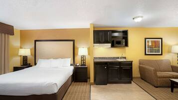 A hotel room with a bed, a nightstand, a desk, a microwave, a sink, and a sofa.