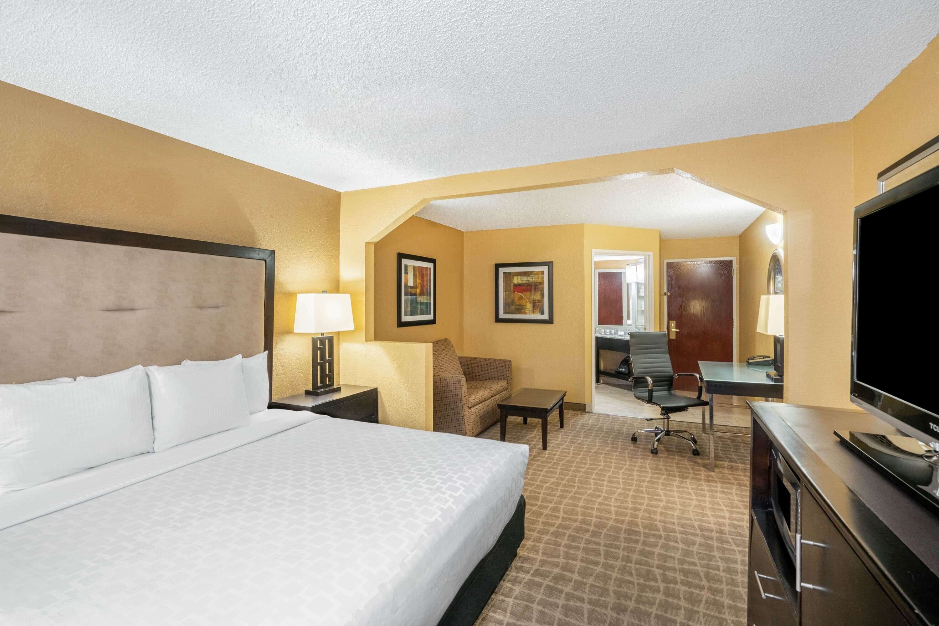A hotel room with a large bed, a desk with a computer, a TV, and a chair.