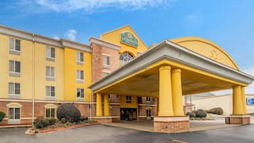 A hotel with a yellow facade, a covered entrance, and a sign reading "La Quinta Inn & Suites".
