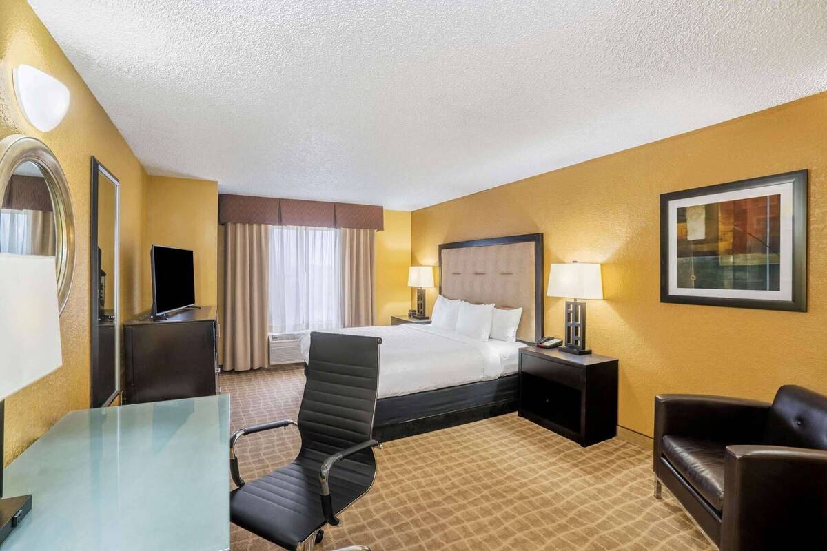 A hotel room with a bed, bedside tables, a desk, a chair, a TV, and a painting on the wall.
