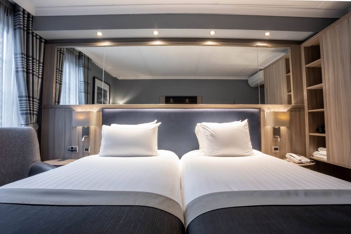 A double bed with white linens, a bedside table with a lamp, and a wardrobe with a mirror.