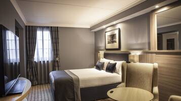 Habitación de hotel con cama, escritorio con una computadora portátil, una silla, una mesita pequeña y un espejo grande.