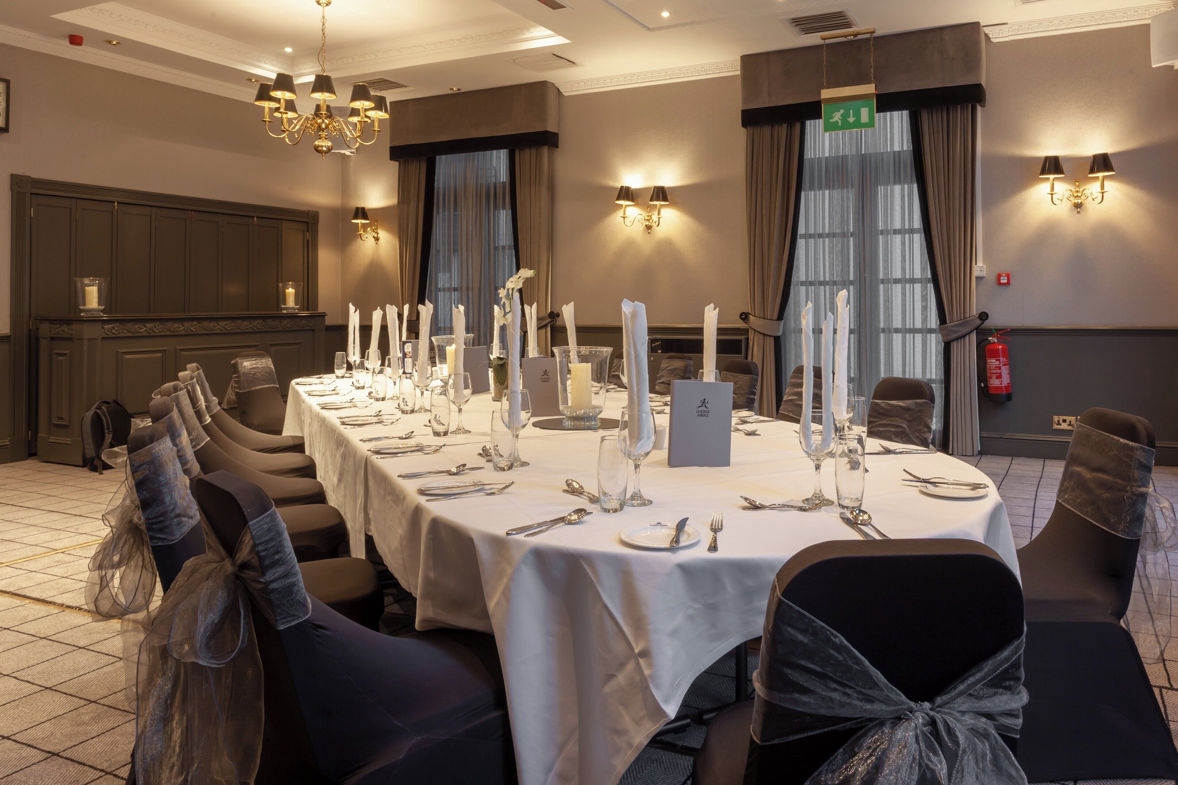 A banquet hall with a long table set for a formal event, equipped with candles, cutlery, and glassware.