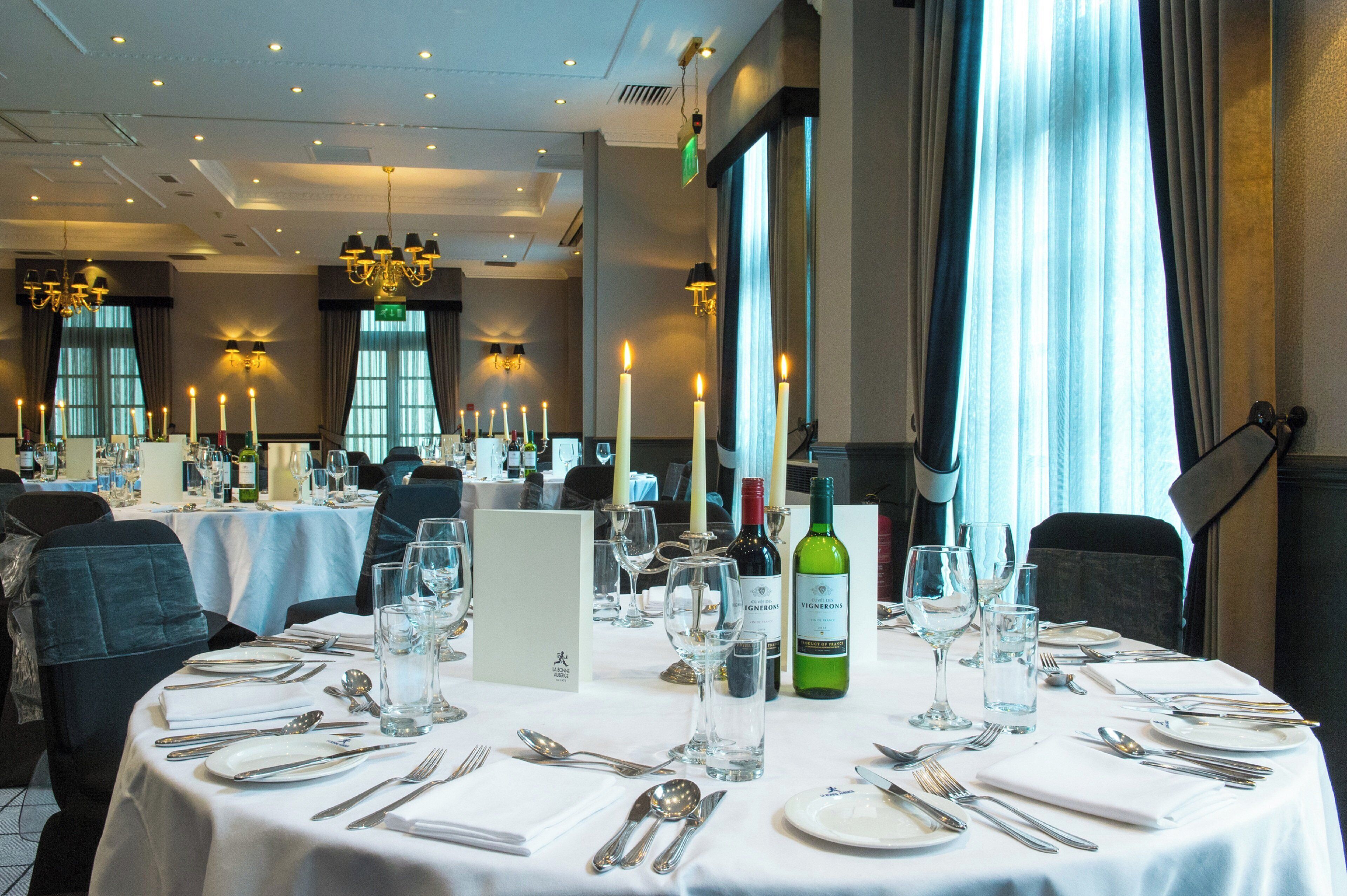 A restaurant setting with tables set for dining, candles, and wine bottles.