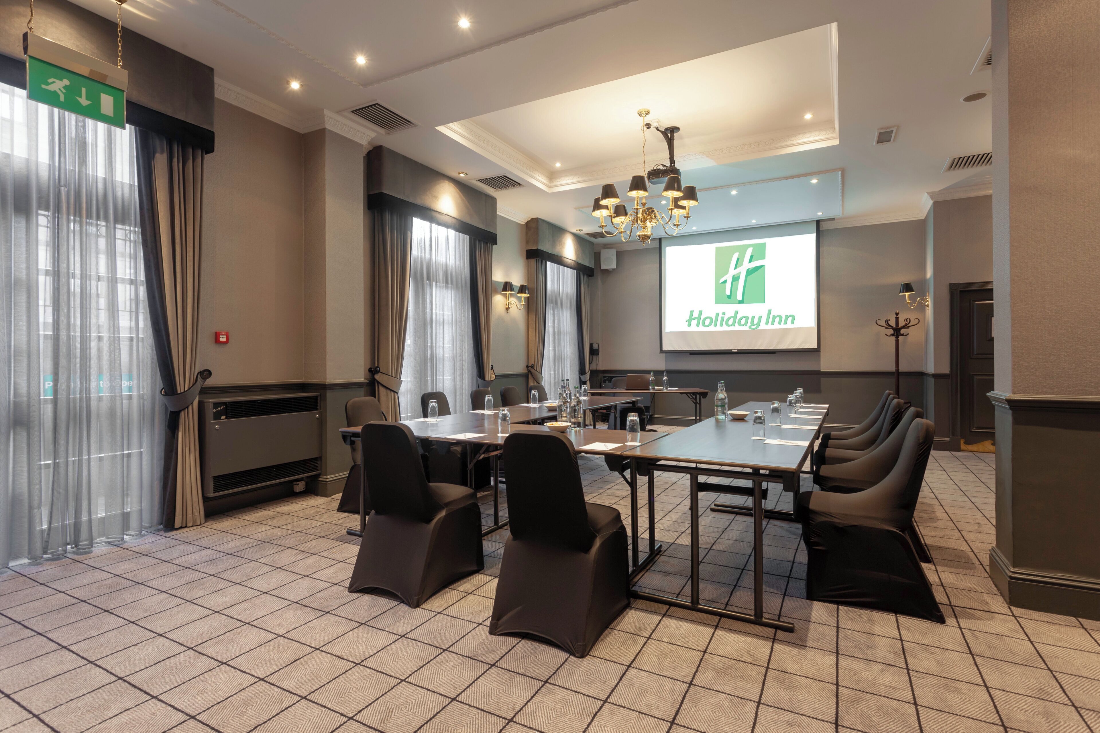 Un salón de conferencias con una amplia mesa, sillas, una pantalla de proyector que muestra el logotipo de un hotel y una araña.
