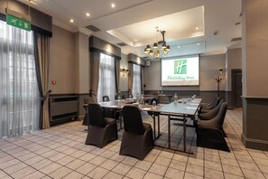 A conference room with a large table, chairs, a projector screen displaying a hotel logo, and a chandelier.