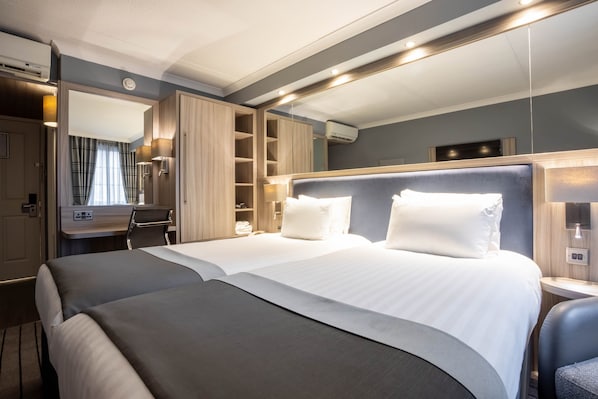 A modern hotel room with a large bed, a desk with a chair, a wardrobe, and a mirror.