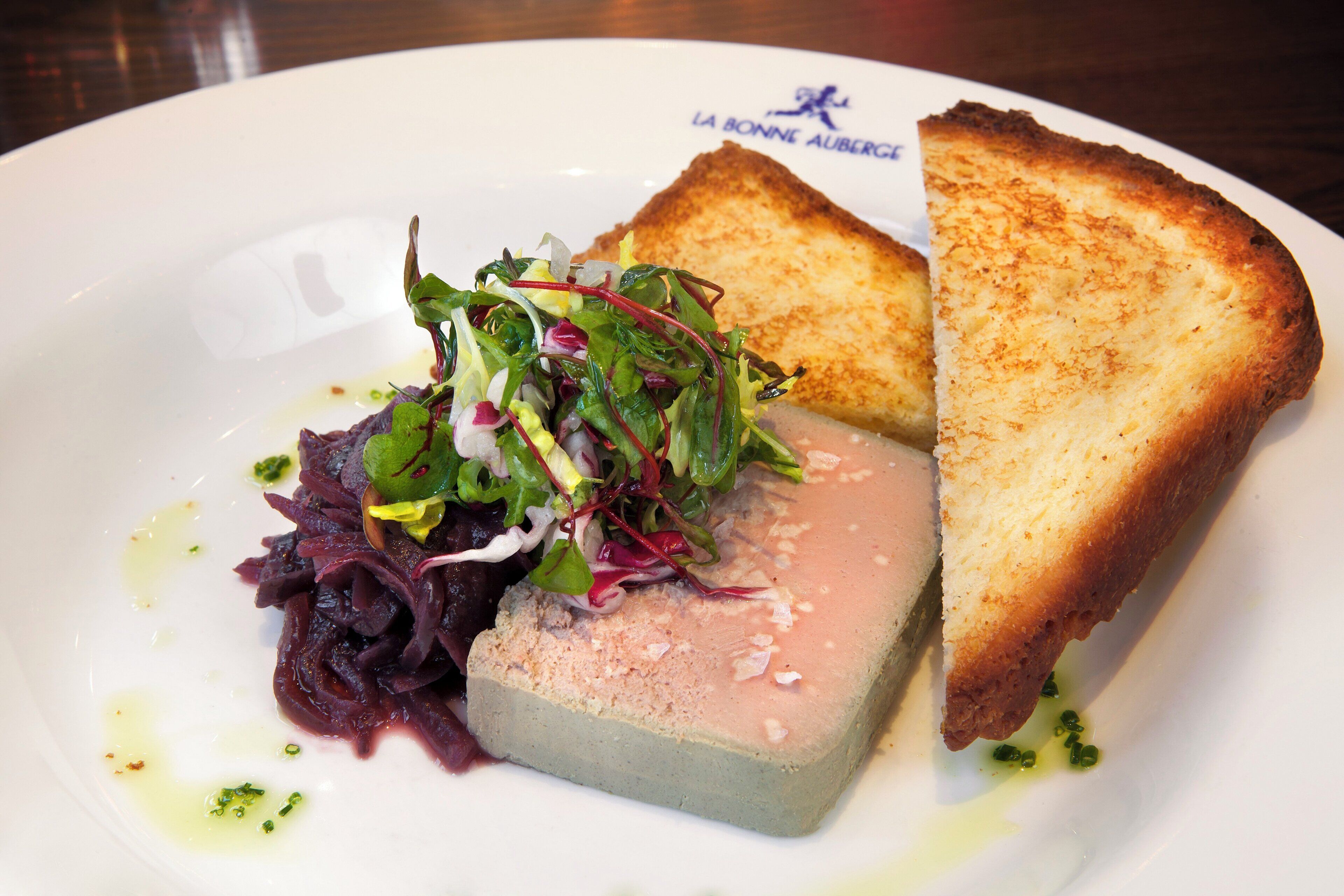 A plate with a slice of toasted bread, a piece of meat, and a salad.