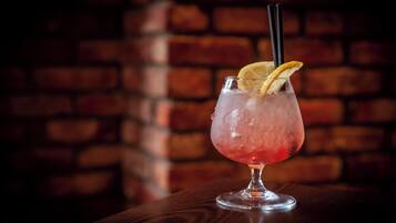 A cocktail glass with a lemon slice garnish on a wooden surface against a brick wall background.
