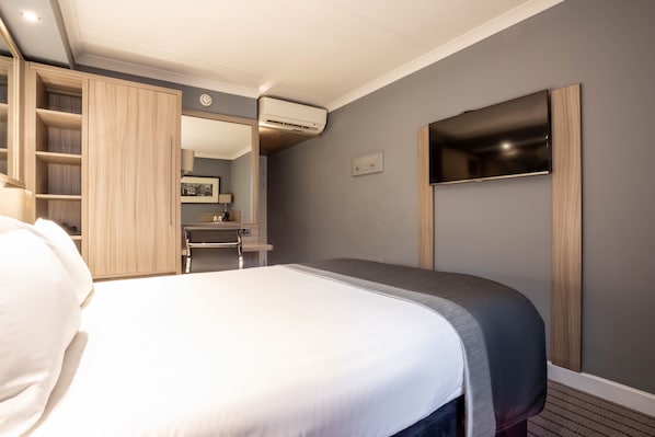 Una habitación de hotel con cama, escritorio, armario y televisor.