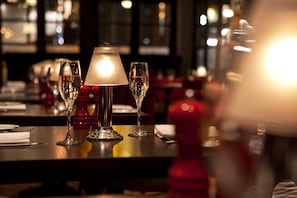 A dining table with a lit table lamp, two wine glasses, and a folded napkin.
