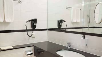 A modern bathroom with a black and white tiled design, a glass shower enclosure, a sink with a soap dispenser, and a telephone.