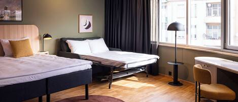 Habitación de hotel con dos camas, un escritorio, una silla, un ventanal grande con cortinas y obras de arte en la pared.