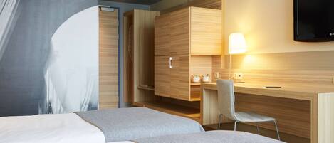 Ein modernes Hotelzimmer mit Bett, Schreibtisch, Stuhl und Fernseher.