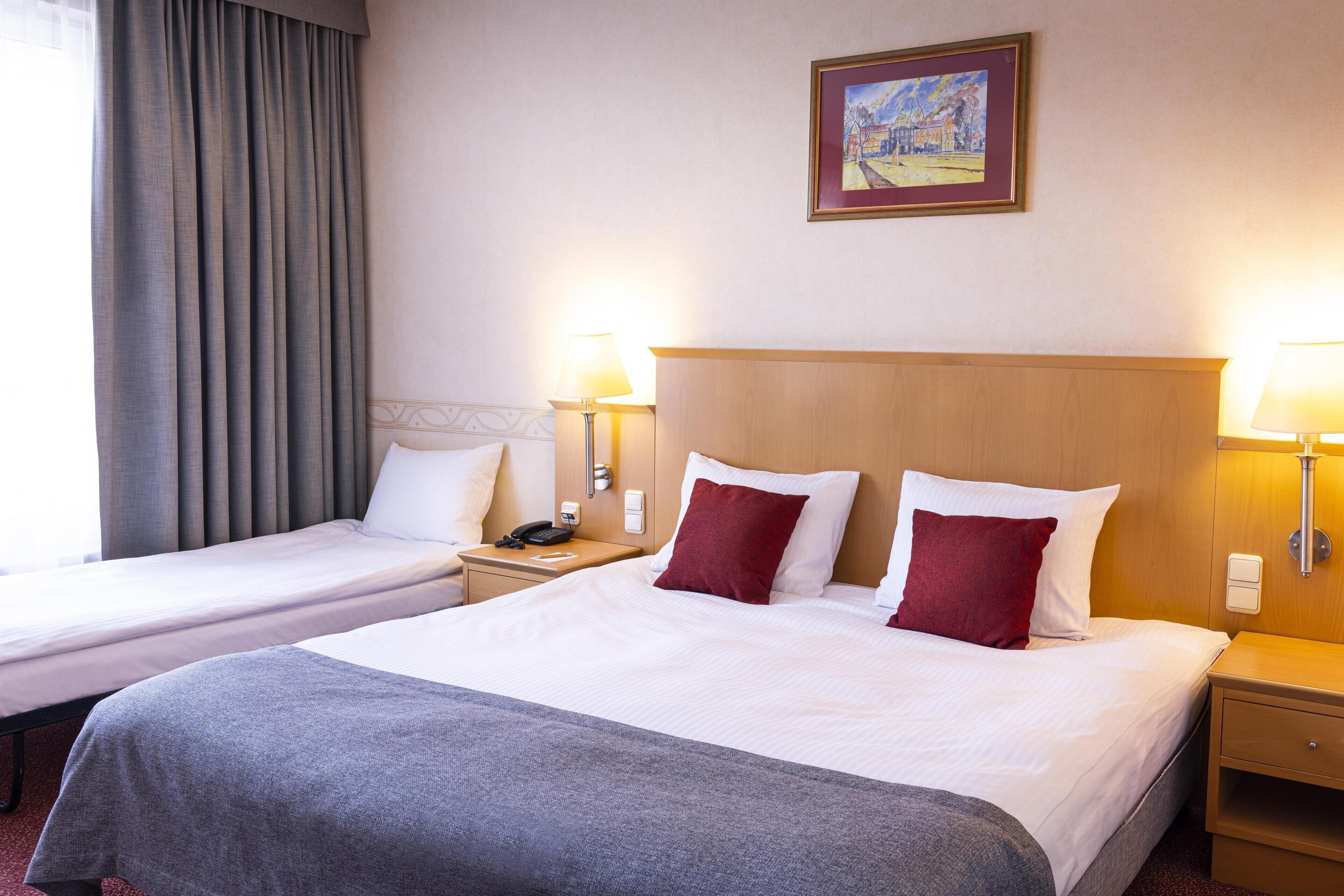 A hotel room with two beds, a painting on the wall, and bedside lamps.