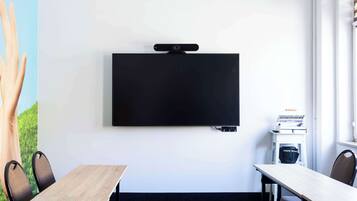A conference room with a mounted flat-screen TV, a wooden table, and two chairs.