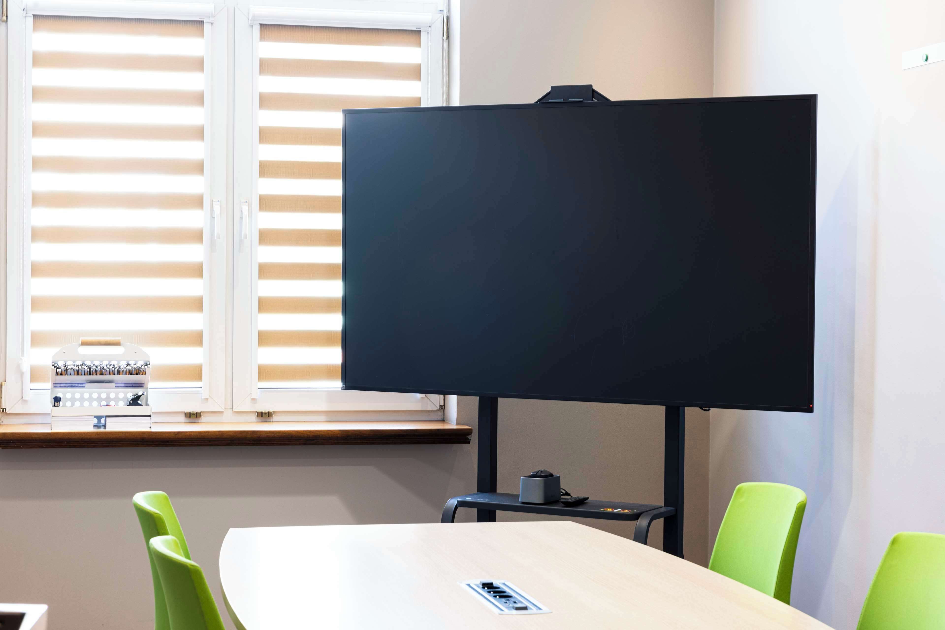 Un salón de conferencias con una pantalla negra grande, sillas verdes y una mesa de madera.