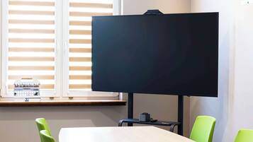 Un salón de conferencias con una pantalla negra grande, sillas verdes y una mesa de madera.