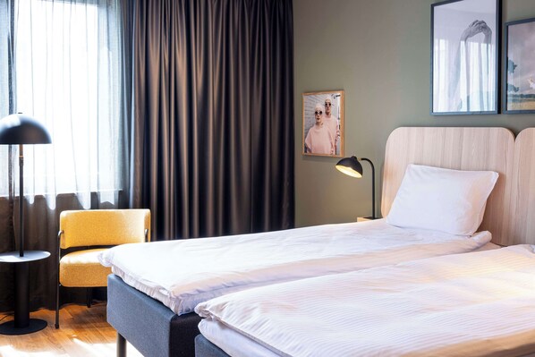 A hotel room with two beds, a chair, a lamp, and a window with curtains. - Scandic Wroclaw (Wroclaw)