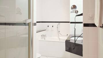 A modern bathroom with a glass shower enclosure, a white bathtub, and a black countertop with a sink.