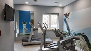 Un gimnasio con cintas de correr, elípticas y un espejo grande.