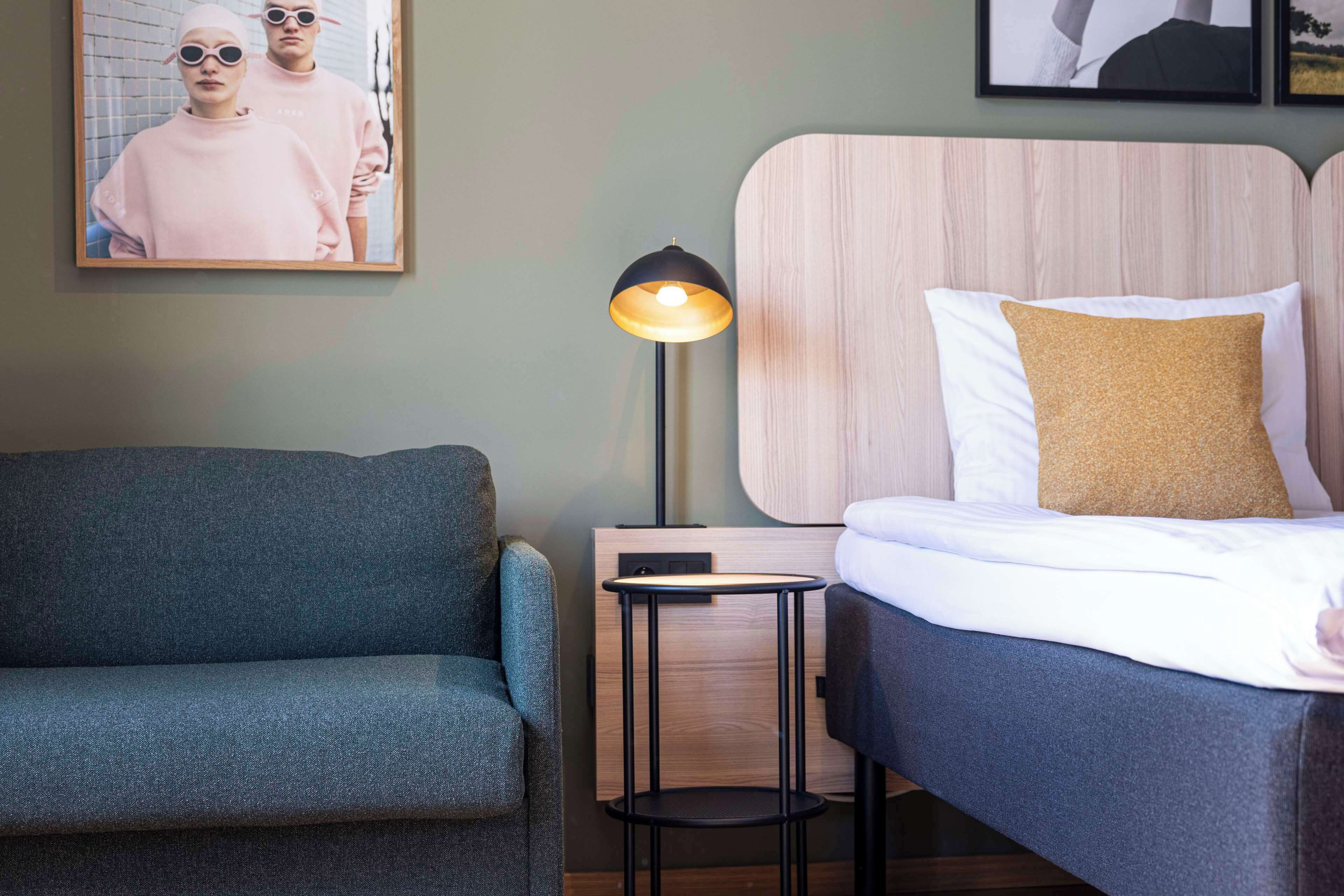 Une chambre à coucher avec un lit, une table de chevet, une lampe, un canapé et un tableau encadré au mur.