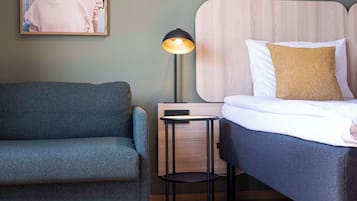 A bedroom with a bed, a side table, a lamp, a sofa, and a framed picture on the wall.