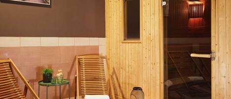 Una sala de sauna con paredes de madera y una puerta de cristal, una silla de madera, una mesita con una planta y un recipiente de vidrio.