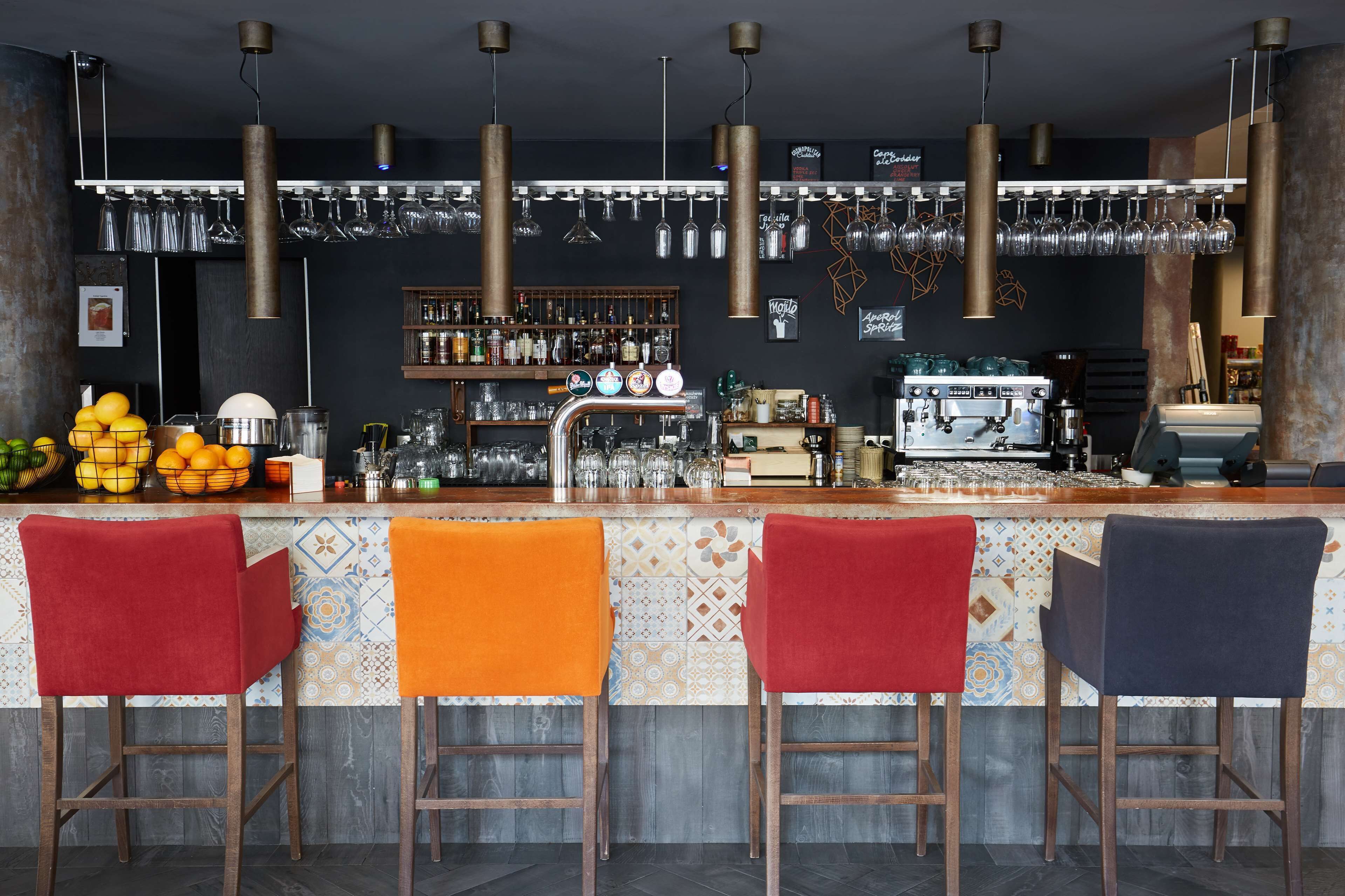 Un espace bar comprenant quatre tabourets, un comptoir, une machine à café, ainsi qu’une variété de verres et de bouteilles.