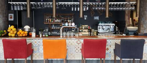 Un espace bar comprenant quatre tabourets, un comptoir, une machine à café, ainsi qu’une variété de verres et de bouteilles.