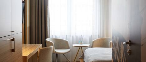A hotel room with a wooden desk, two chairs, a small round table with a bottle, and a bed.
