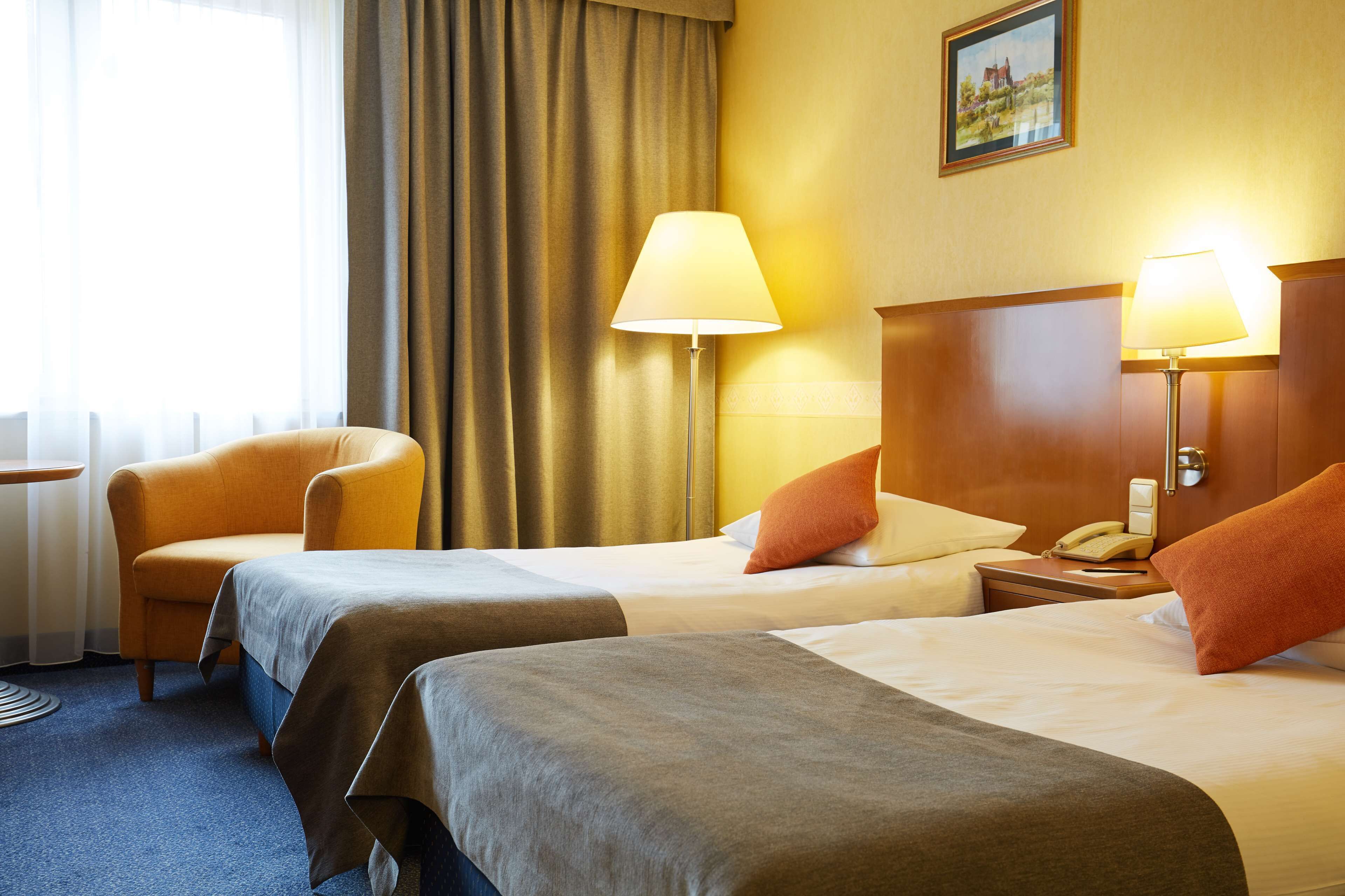 A hotel room with two beds, a chair, a desk, and a lamp.