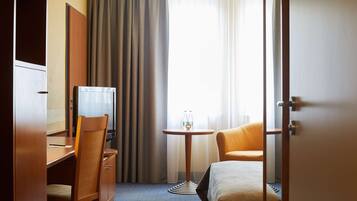 Une chambre d’hôtel comprenant un lit, un bureau avec une chaise, une télévision et une petite table avec deux bouteilles.
