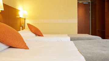 Une chambre d’hôtel avec deux lits, chacun étant équipé de draps blancs et d’oreillers orange. Une table de chevet avec une lampe se trouve sur le côté gauche de chaque lit.
